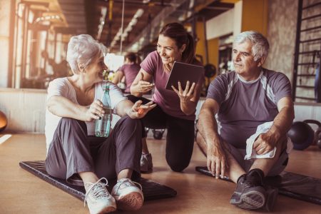 Senior couple in rehabilitation center. Personal trainer showing something on digital tablet.